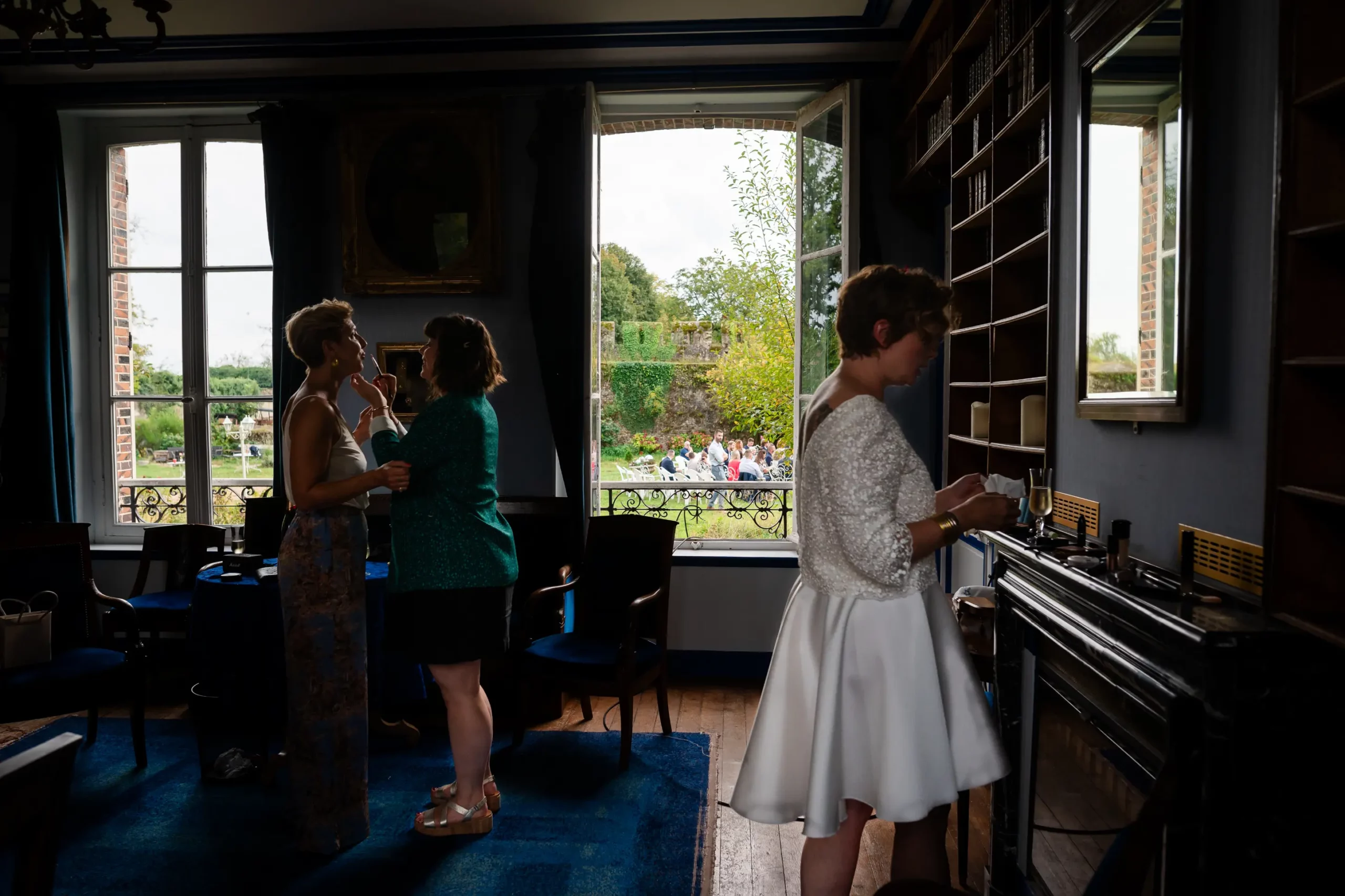 photojournaliste de mariage, pendant les préparatifs de la mariée en premier plan et en arrière plan on voit par la fenêtre les invités qui attendent sur le lieu de la cérémonie laïque